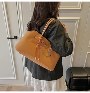 Detail of a large orange leather tote bag with woven knots and metallic heart charm