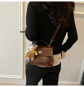 Detail of glossy dark brown crossbody bag with gold lock and cute teddy bear charm