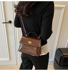 Detail of a shiny brown leather crossbody bag with vintage gold swivel lock worn by a model