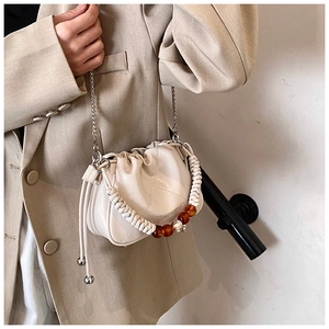 Detail of beige pleated cloud bag with woven handle and amber bead accents