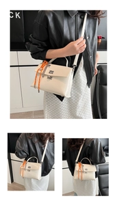 Detail of off-white messenger bag featuring a silver twist lock and orange braided charm