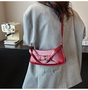 Detail of red crescent shoulder bag with silver buckle worn by a model in a grey blazer