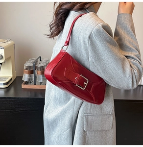 Detail of red patent leather underarm bag with shiny finish and metal buckle strap