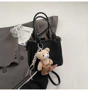 Detail of black lychee grain bucket bag with dual knot handles and cute bear pendant