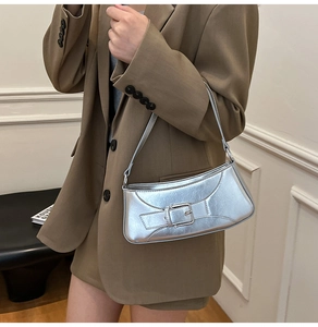 Shoulder carry view of a silver baguette bag with a stylish metal buckle strap detail