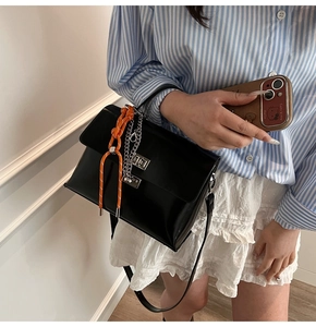 Detail of black glossy handbag featuring vibrant orange accent cord and silver buckle