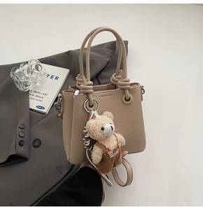 Detail of beige lychee texture handbag with knotted handle and cute bear charm pendant
