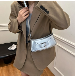 Detail view of silver baguette bag with metallic buckle on a model wearing a blazer