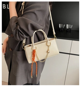 Détail d'un sac à main en similicuir blanc cassé avec chaîne dorée et pendentif tissé