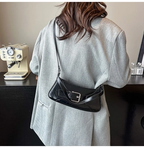 Detail of glossy black shoulder bag with silver buckle worn by model in a cafe setting