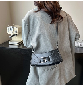Detail of black crescent shoulder bag with glossy leather and metallic buckle on model