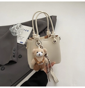 Close-up of beige lychee texture bucket bag with woven handle and plush bear charm