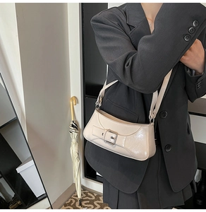 Detail of cream baguette bag with glossy leather texture and buckle on suit jacket