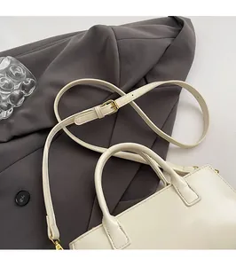 Détail d'un sac en cuir crème avec bandoulière réglable et boucles dorées sur veste