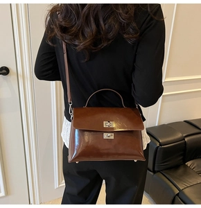 Detail of glossy brown leather crossbody bag with silver square twist lock and top handle
