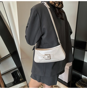 Detail view of cream white patent leather shoulder bag with metallic buckle and strap