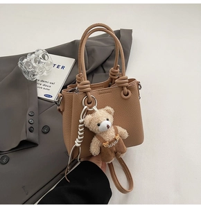 Detail view of camel lychee pattern bucket bag with a cute teddy bear plush charm