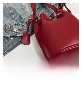 Detail of dark red lychee leather bucket bag featuring a metal buckle and fine shoulder strap