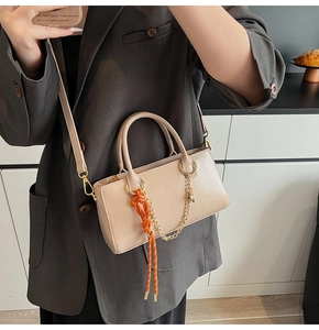 Détail du sac à main beige en cuir ciré avec chaîne dorée et pendentif tissé orange vif