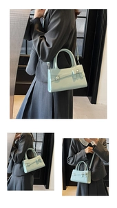 Detail of mint green handbag featuring decorative belt buckle and bow styling with strap