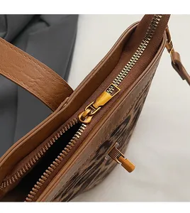 Close-up of smooth gold metal zipper and brown leather trim on leopard print tote bag