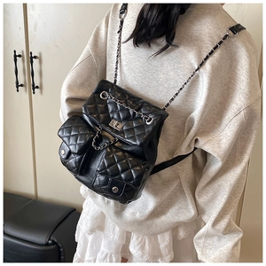 Detail of black quilted leather backpack with silver chain straps worn by a female model