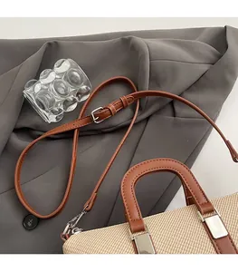 Detail of woven straw and brown leather bucket bag with adjustable shoulder strap