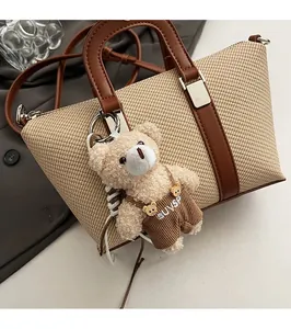 Detail of beige woven bucket bag featuring brown leather handles and a cute plush bear charm