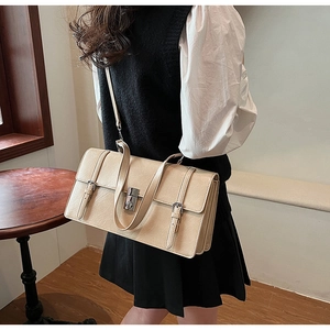 Detail of a beige leather shoulder bag with silver turn-lock and decorative buckle straps
