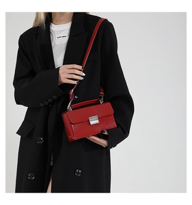 Detailansicht der roten Lackleder-Handtasche mit silbernem Schloss auf schwarzem Blazer
