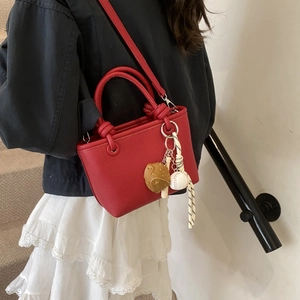 Dettaglio in primo piano dell'elegante borsa a secchiello rossa con manico e ciondoli.