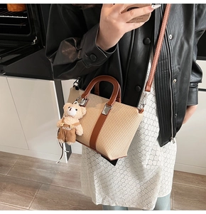 Detail of beige woven bucket bag with brown leather handles and cute plush bear charm