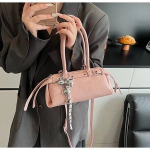 Pink cylinder boston bag with bow and heart charms held by model in casual suit