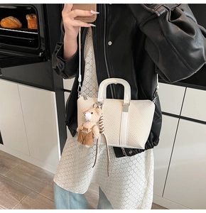 Detailed shot of white textured bucket bag with teddy bear charm and silver hardware