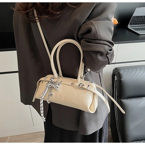 Detail shot of a cream Boston bag with silver bow charm worn by a model in a modern room