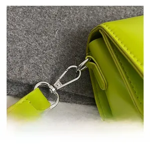 Detail of silver metal hook and smooth bright green PU leather on a small crossbody bag
