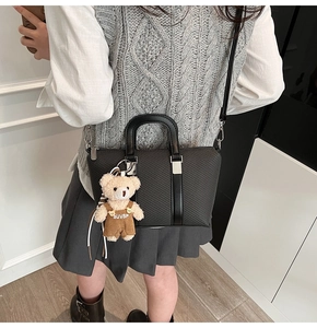 Detail of black woven shoulder bag with plush bear charm and crossbody strap