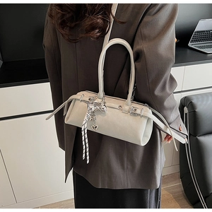 Close-up of cream leather Boston bag with silver bow pendant and woven rope knot detail