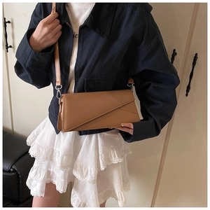Detail of brown leather crossbody bag with diagonal flap and adjustable strap on model