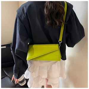 Detail of lime green asymmetric envelope crossbody bag on a model with blue jacket