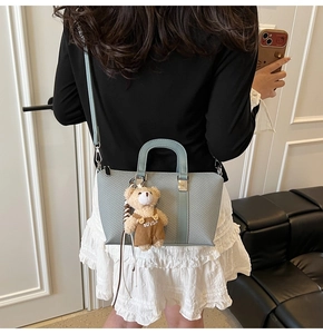 Close-up of light blue textured bucket bag with teddy bear charm worn by model