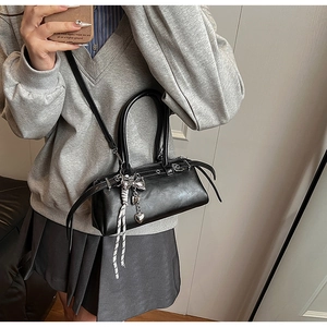 Detail of a black Boston bag with silver bow and heart chain charms on a shoulder strap