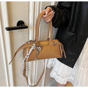 Close-up of caramel Boston bag with silver bow charm and striped rope handle details