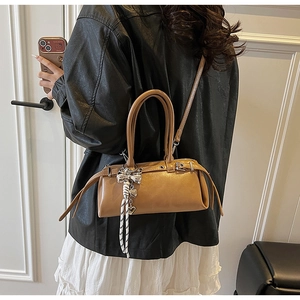 Side view of caramel leather Boston bag with decorative charm and shoulder strap