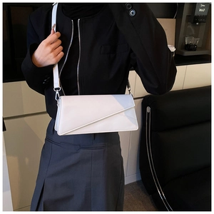 Détail d'un sac à bandoulière blanc minimaliste avec un rabat asymétrique et boucle