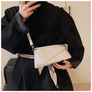 Close-up of minimalist beige crossbody bag with geometric flap on a black coat