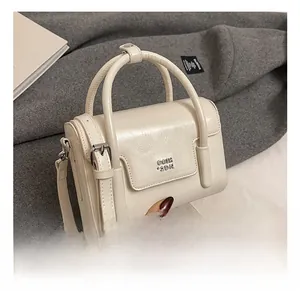 Detail of a beige leather handbag with metal logo on textured grey fabric