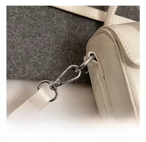 Detail of silver metal swivel hook and glossy white leather strap connection on small bag