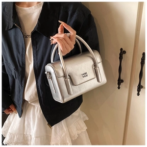 Detail of silver metallic wrinkled texture and embossed logo on minimalist square handbag