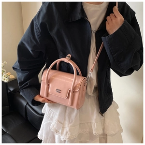 Detail showing high-gloss light pink patent leather texture and silver logo of the bag